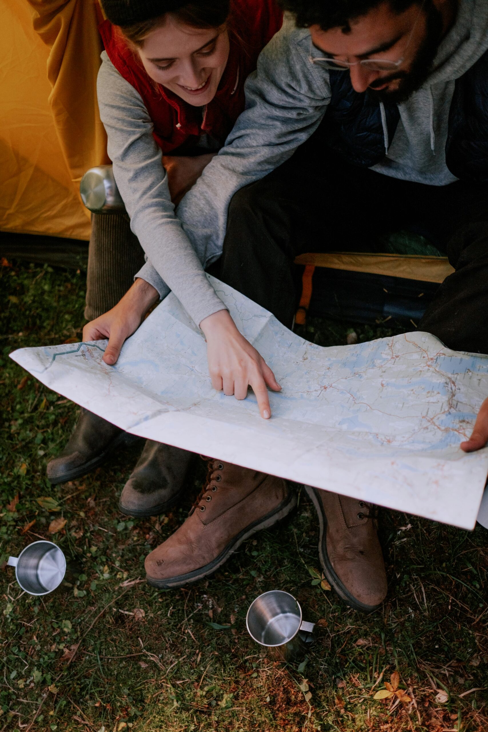 Couple sitting near tent pointing at map, planning adventure.